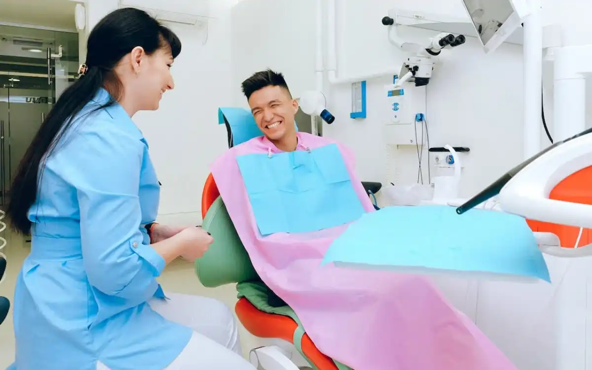 Female dentist and a male patient smiling to each other inside a dental clinic.